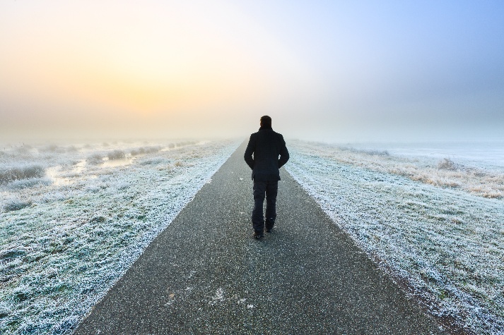 A solitary figure walking along a pale frozen road toward the horizon
