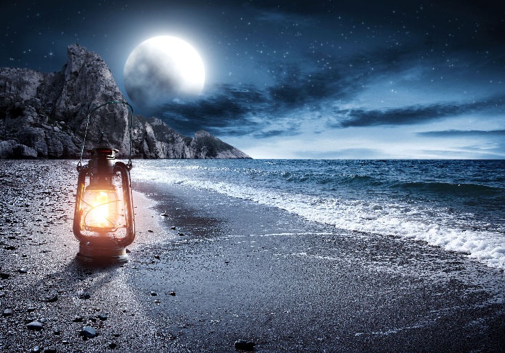 A glowing lantern on a moonlit beach beneath a deep blue sky