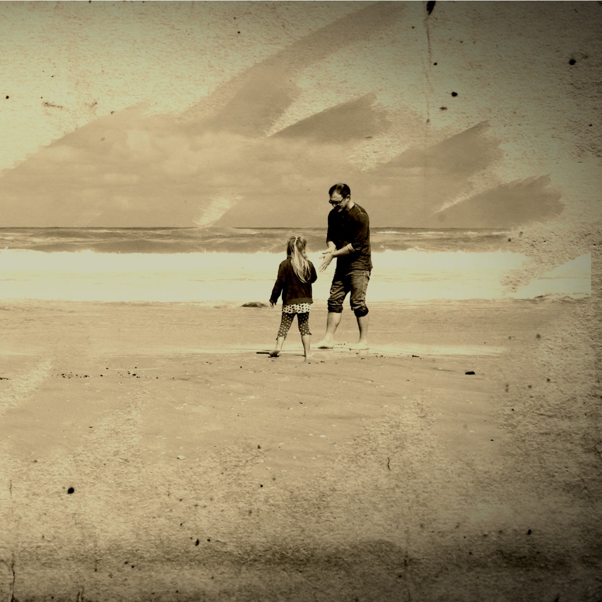 A father and young child walking together on a beach in a sepia-toned image
